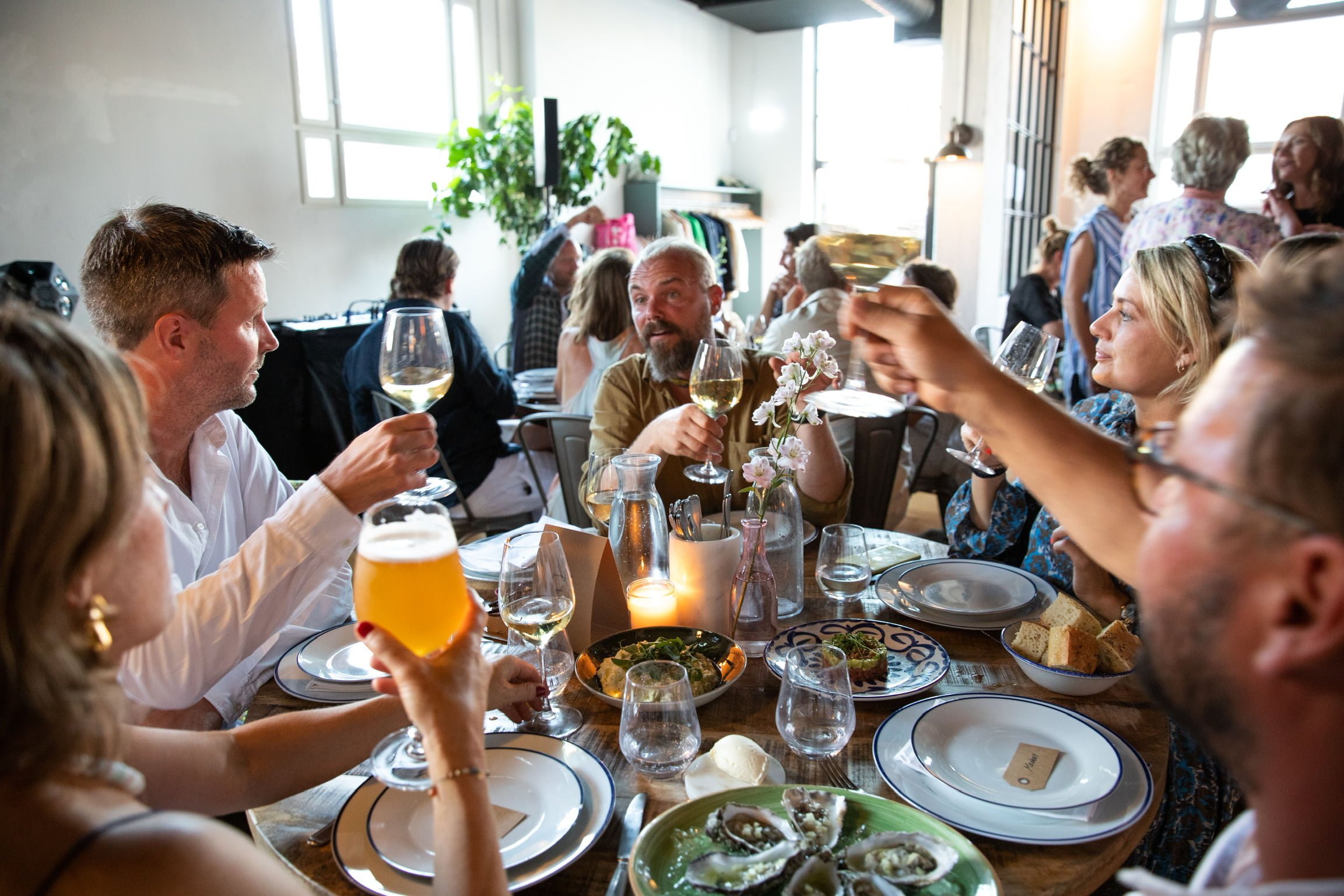 Foto af en gruppe mennesker der sidder rundt om et bord i restaurant Lindgreens og skåler