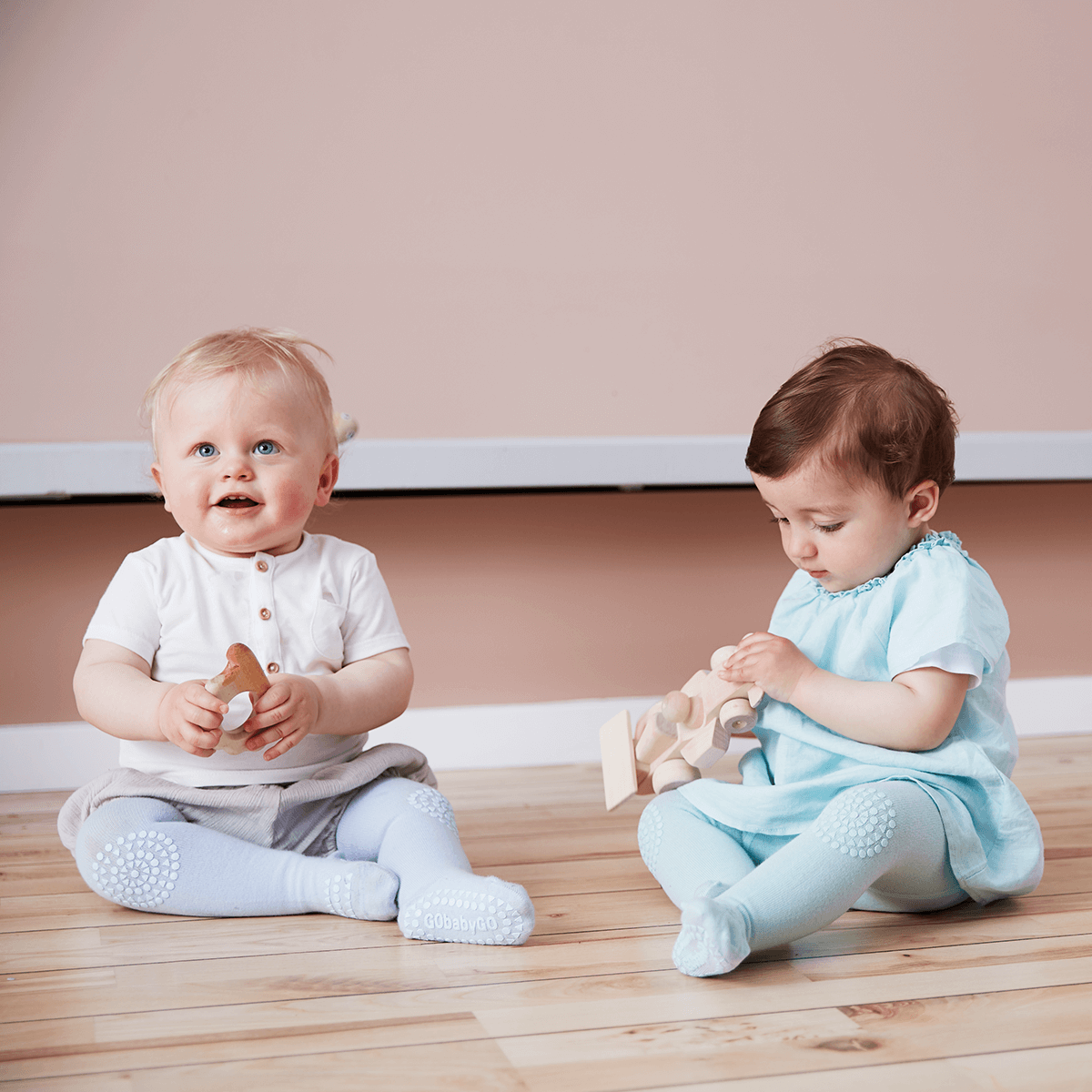 Billede af 2 babyer der sidder på gulvet og leger med legetøj.