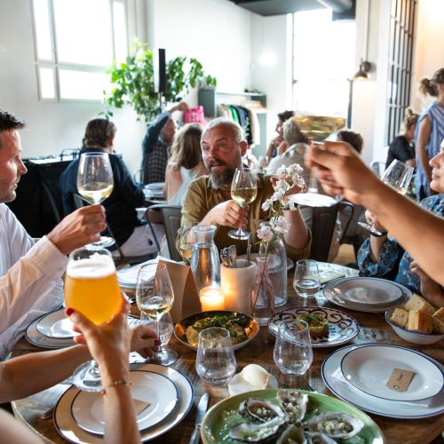 Foto af en gruppe mennesker der sidder rundt om et bord i restaurant Lindgreens og skåler
